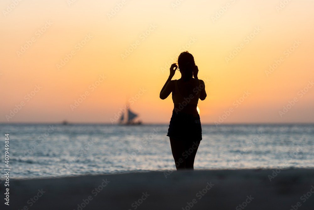 (Selective focus) Stunning view of the silhouette of a girl walking on a beach during a beautiful and romantic sunset. White Beach, Boracay Island, Philippines.