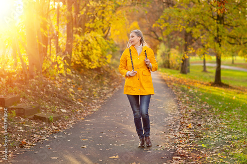 Weißhaarige Grauhaarige Frau spaziert im Park Herbst Sonnenstrahlen gelbe Regenmantel  © Anastasia