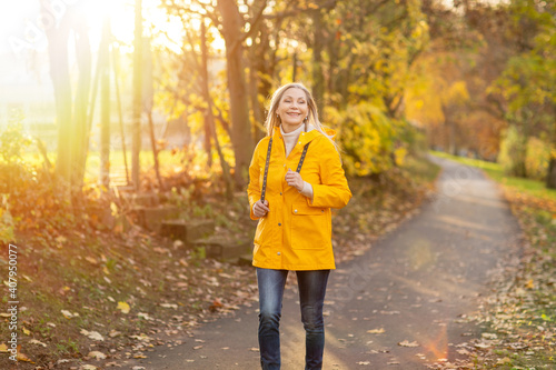 Wei  haarige Grauhaarige Frau spaziert im Park Herbst Sonnenstrahlen gelbe Regenmantel 