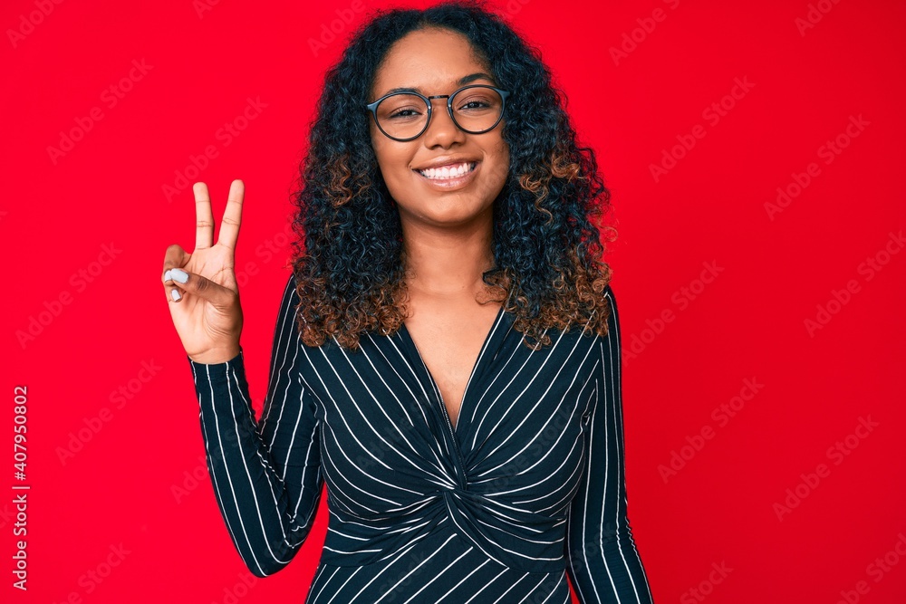 Young african american woman wearing casual clothes and glasses smiling with happy face winking at the camera doing victory sign. number two. Young african american woman wearing casual clothes and glasses smiling with happy face winking at the camera doing victory sign. number two.