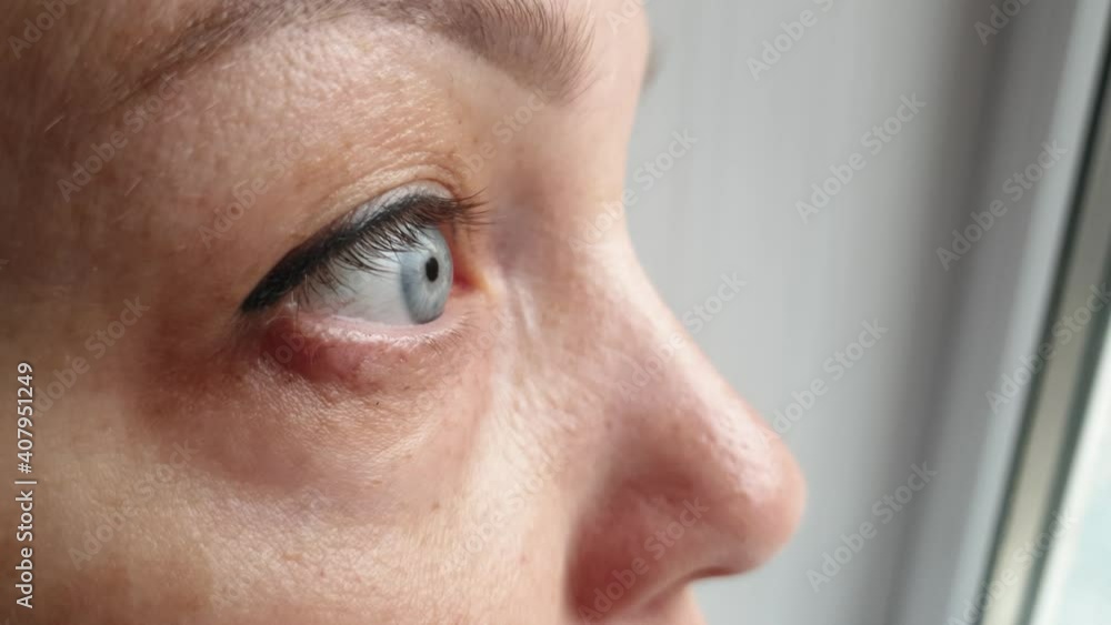 a woman in quarantine in self isolation wearing a medical mask looks out the window