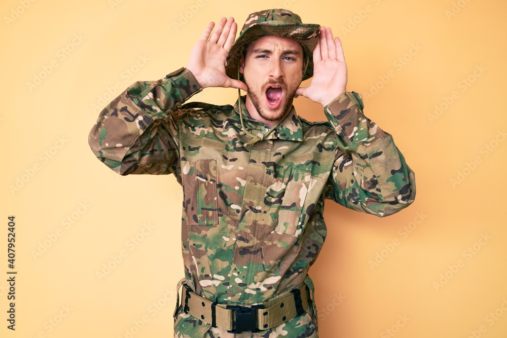 Young caucasian man wearing camouflage army uniform smiling cheerful playing peek a boo with hands showing face. surprised and exited Young caucasian man wearing camouflage army uniform smiling cheerful playing peek a boo with hands showing face. surprised and exited