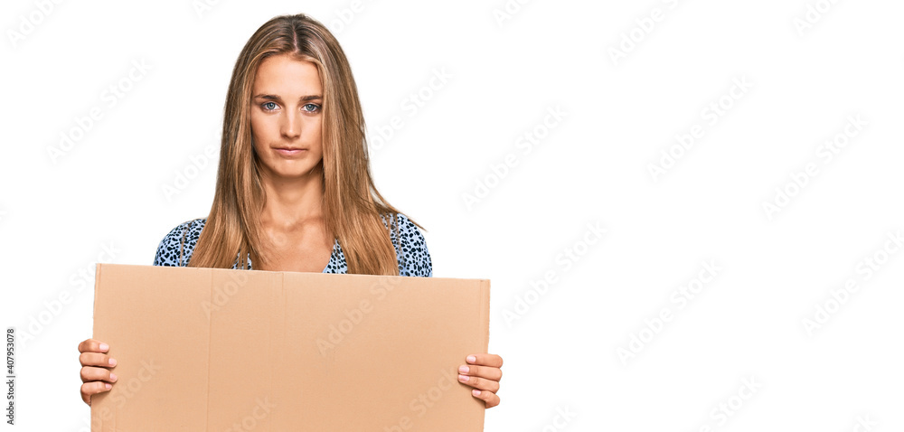 Young blonde woman holding cardboard empty banner thinking attitude and sober expression looking self confident Young blonde woman holding cardboard empty banner thinking attitude and sober expression looking self confident