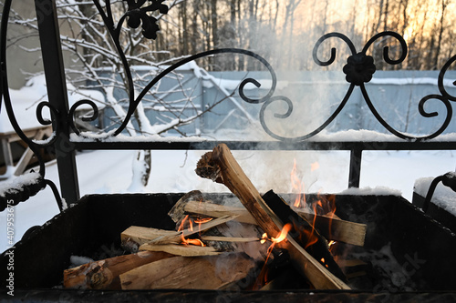 Close-up of burning and smoking wood in wrought iron brazier at winter. Safe fire. Outdoors cooking.