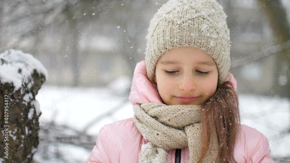 Winter portrait of a kid girl in pink coat wearing beige hat and mittens playing outdoor in snowy winter forest and blowing snow. Happy childhood and active holidays concept Winter portrait of a kid girl in pink coat wearing beige hat and mittens playing outdoor in snowy winter forest and blowing snow. Happy childhood and active holidays concept
