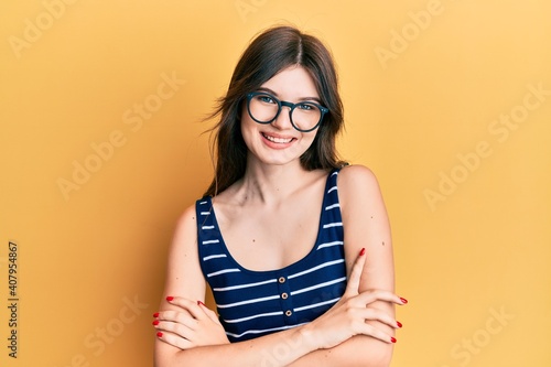 Young beautiful caucasian girl wearing casual clothes and glasses happy face smiling with crossed arms looking at the camera. positive person.