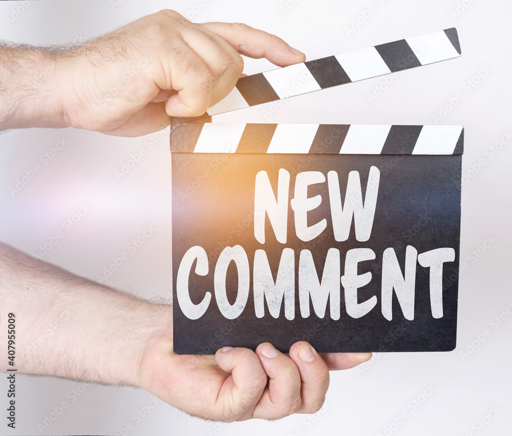 Obraz premium On a white background, a man holds a clapperboard in his hands on which it is written - NEW COMMENT