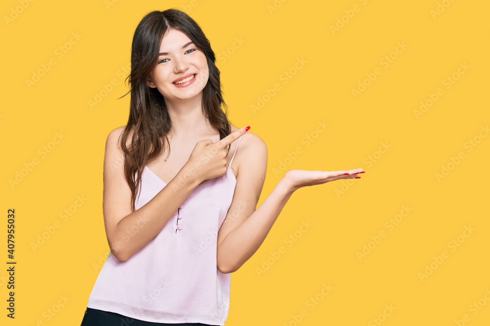 Young beautiful caucasian girl wearing casual clothes amazed and smiling to the camera while presenting with hand and pointing with finger. Young beautiful caucasian girl wearing casual clothes amazed and smiling to the camera while presenting with hand and pointing with finger.