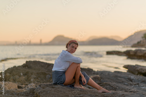 Young pretty caucasian woman in white shirt and gray skirt having fun on the rocks by the sea shore