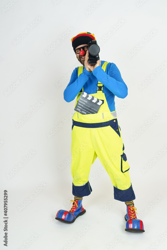 A clown in bright clothes is filming with a movie camera. Isolated on white A clown in bright clothes is filming with a movie camera. Isolated on white