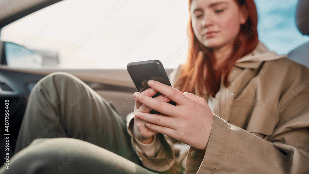 Portrait of teenage girl looking at the screen while using her phone, sitting in the car. Smartphone addiction concept
