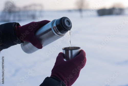 Pouring hot water frm thermos to cup in winter, winter sunrise or sunset, very cold weather, visible steam