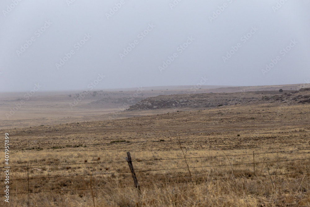 Dreamy shot of rocky hills with plateaus in open yellow field in rural New Mexico on cloudy day
