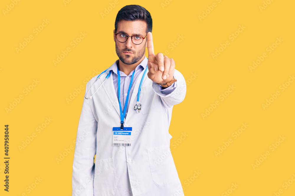 Young hispanic man wearing doctor uniform and stethoscope pointing with finger up and angry expression, showing no gesture Young hispanic man wearing doctor uniform and stethoscope pointing with finger up and angry expression, showing no gesture