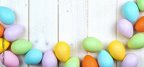 Several bright color dyed Easter eggs on wooden background in flat lay with copy space. Border for Happy Easter minimal concept card or banner