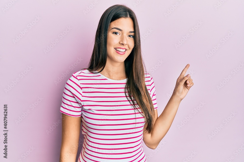Young brunette woman wearing casual clothes over pink background with a big smile on face, pointing with hand finger to the side looking at the camera.