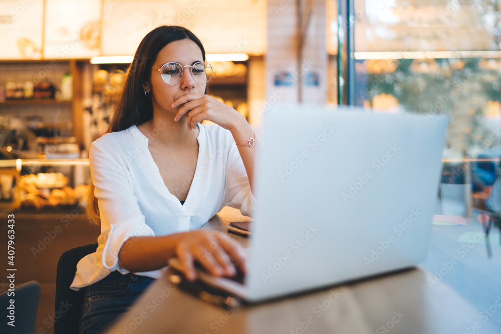 Professional business women in casual wear and glasses for vision correction browsing web page and reading information during remote job, pretty young female student millennial watching webinar