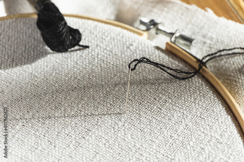 Needle and thread on white fabric inside embroidery hoop