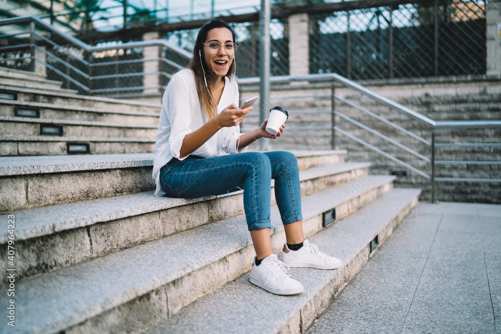 Smiling woman using phone while sitting on outdoor stairs Smiling woman using phone while sitting on outdoor stairs