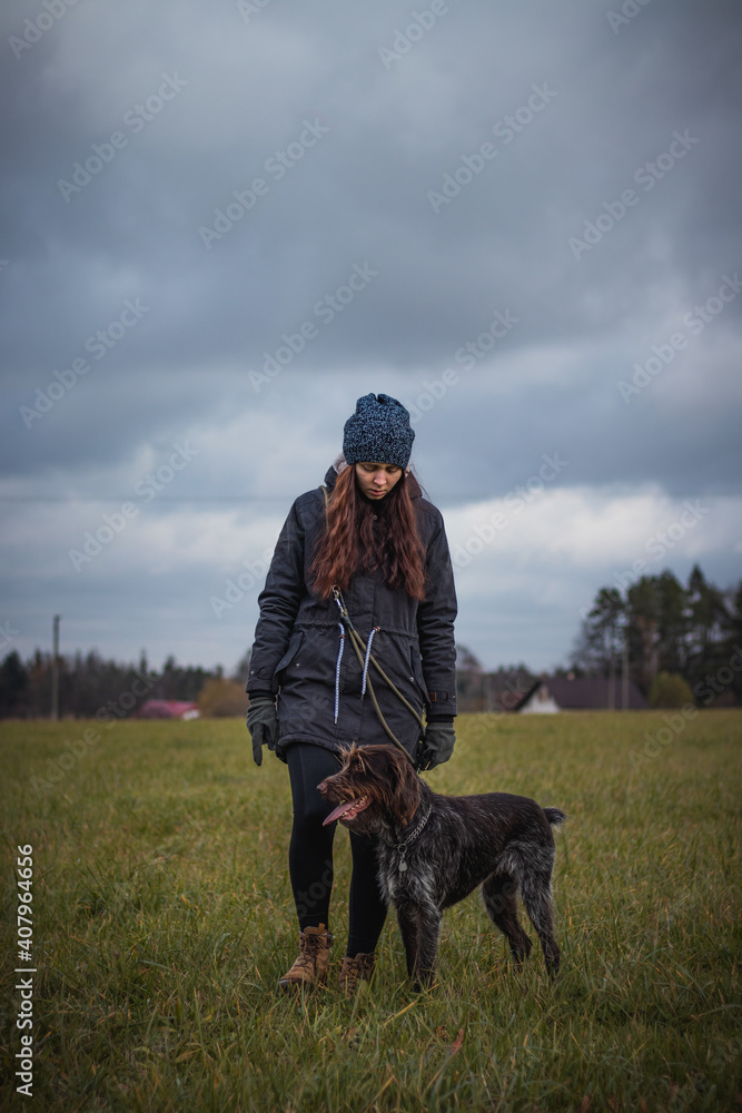 Walking a young girl in winter clothes and brown-and-white Bohemian Wire-haired Pointing Griffon in an approaching thunderstorm. Binary portrait of a woman and a cute dog at Grey Moss tone Walking a young girl in winter clothes and brown-and-white Bohemian Wire-haired Pointing Griffon in an approaching thunderstorm. Binary portrait of a woman and a cute dog at Grey Moss tone
