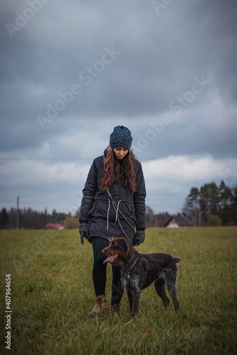 Walking a young girl in winter clothes and brown-and-white Bohemian Wire-haired Pointing Griffon in an approaching thunderstorm. Binary portrait of a woman and a cute dog at Grey Moss tone