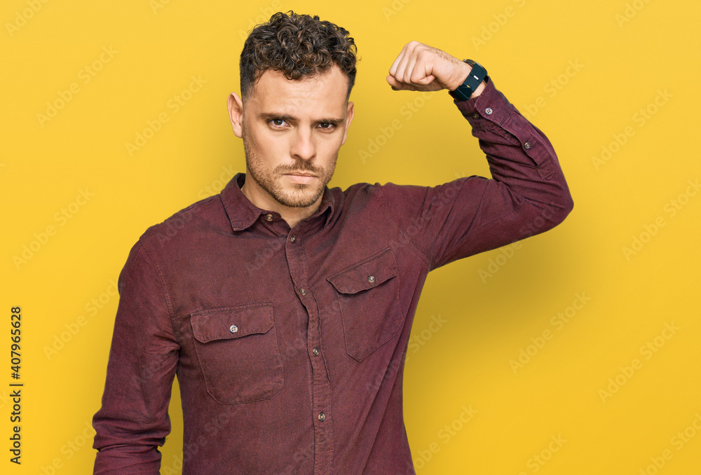Young hispanic man wearing casual clothes strong person showing arm muscle, confident and proud of power Young hispanic man wearing casual clothes strong person showing arm muscle, confident and proud of power
