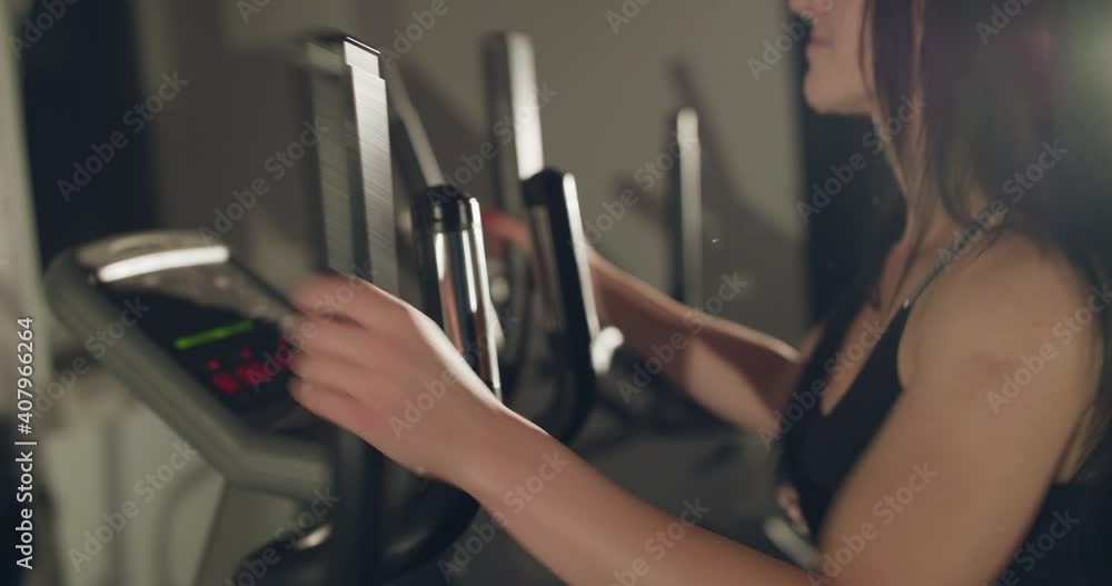 Side view of happy woman working out on exercise spin bike in gym with backlit Side view of happy woman working out on exercise spin bike in gym with backlit