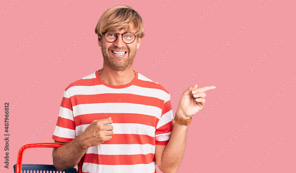 Handsome caucasian man with beard holding supermarket shopping basket smiling happy pointing with hand and finger to the side Handsome caucasian man with beard holding supermarket shopping basket smiling happy pointing with hand and finger to the side