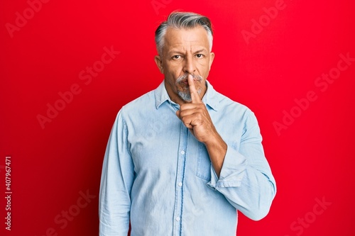 Middle age grey-haired man wearing casual clothes asking to be quiet with finger on lips. silence and secret concept.