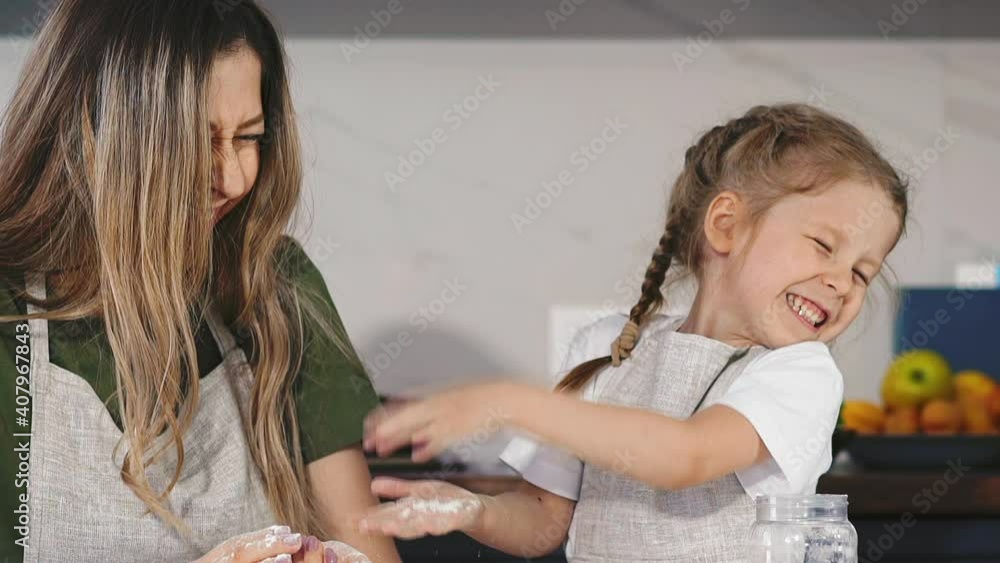 slow motion, close up: young mother and young daughter have a lot of fun in kitchen when they cook together, laugh, fun, child claps hands in which flour is saved in front of mother, fearing slow motion, close up: young mother and young daughter have a lot of fun in kitchen when they cook together, laugh, fun, child claps hands in which flour is saved in front of mother, fearing