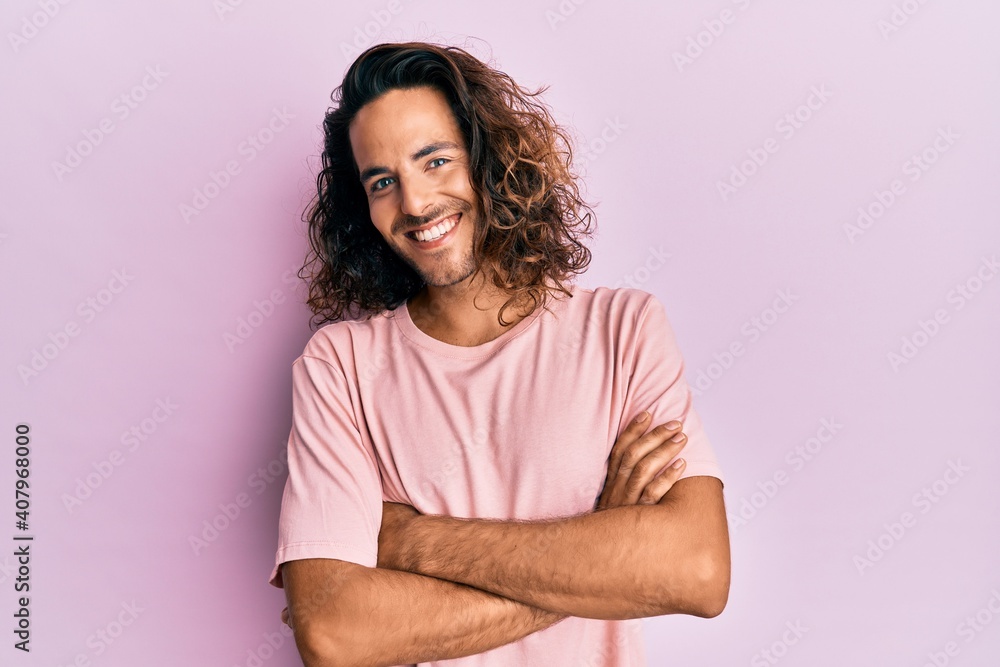 Young handsome man with long hair wearing casual clothes happy face smiling with crossed arms looking at the camera. positive person. Young handsome man with long hair wearing casual clothes happy face smiling with crossed arms looking at the camera. positive person.