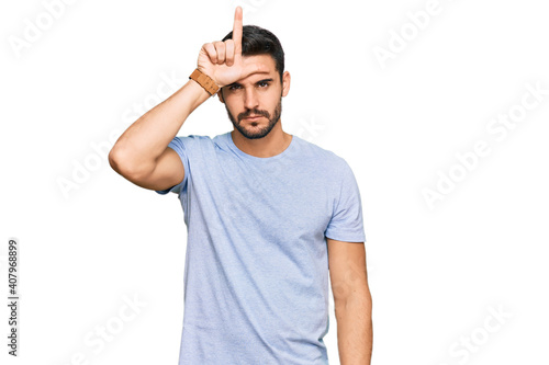 Young hispanic man wearing casual clothes making fun of people with fingers on forehead doing loser gesture mocking and insulting.