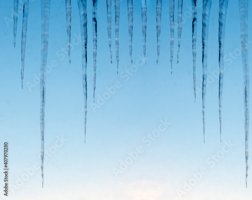 Background of bright transparent icicles in the sunlight. Icicles on the sky background. Copy space. Winter. Nature.