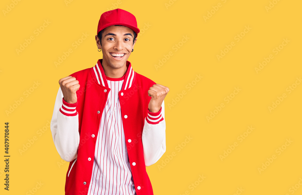 Young african amercian man wearing baseball uniform celebrating surprised and amazed for success with arms raised and open eyes. winner concept. Young african amercian man wearing baseball uniform celebrating surprised and amazed for success with arms raised and open eyes. winner concept.