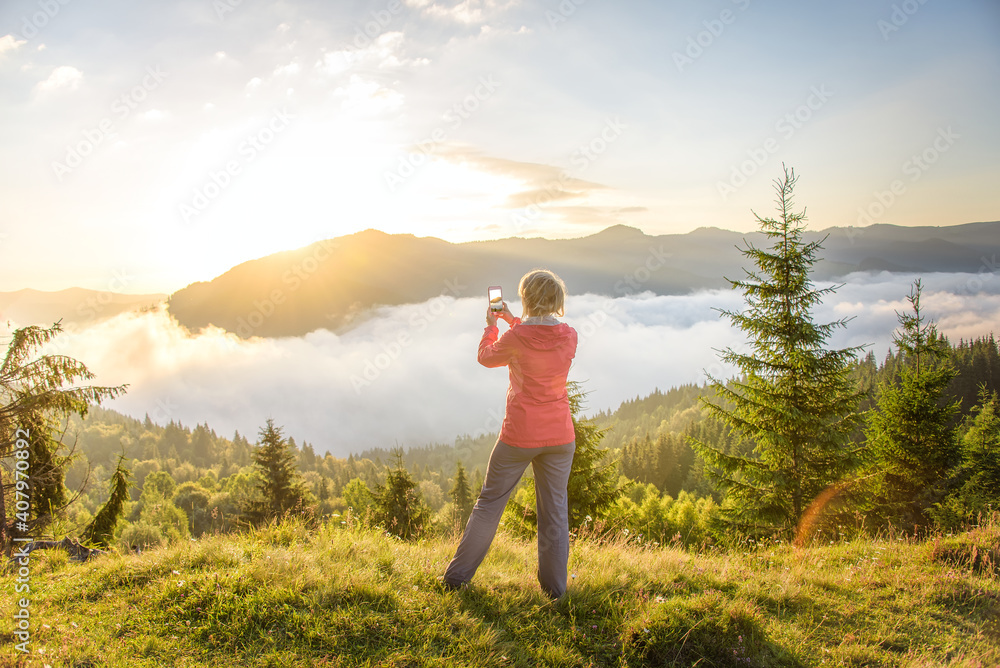 The girl photographs the sunrise in the mountains. A tourist girl at the top of the mountain photographs the rising sky.