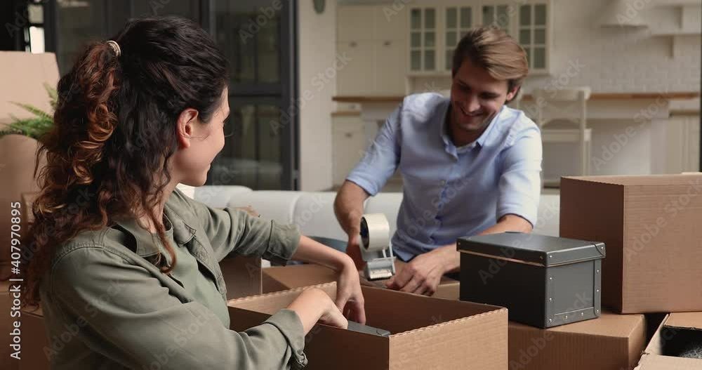 Happy young european married couple unpacking together belongings from huge carton boxes, moving into new house, feeling excited of purchasing own apartment or relocation renovation processes. Happy young european married couple unpacking together belongings from huge carton boxes, moving into new house, feeling excited of purchasing own apartment or relocation renovation processes.