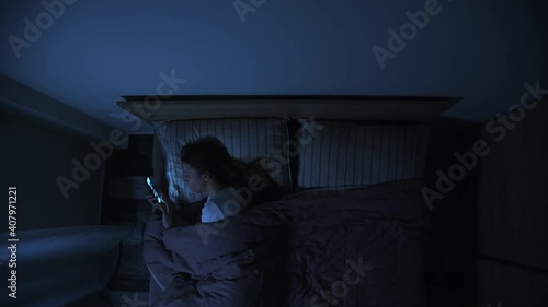 Top view of one woman in bed at night looking at her smartphone, female insomnia problem, woman can not get asleep at night, lonely girl in bed at night.