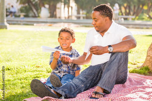 Happy African American Father and Mixed Race Son Playing with Paper Airplanes in the Park