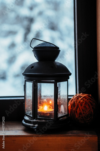 lantern with burning candle on the windowsill with a winter view.