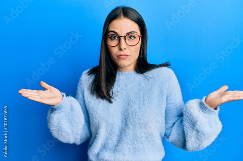 Young brunette woman wearing casual clothes and glasses clueless and confused with open arms, no idea and doubtful face.