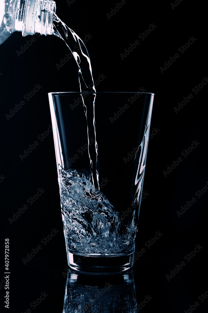 In a transparent glass on a black background pouring water from the bottle. In a transparent glass on a black background pouring water from the bottle.