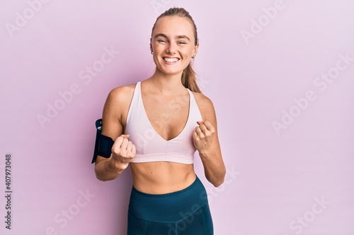Beautiful blonde woman wearing sportswear and arm band very happy and excited doing winner gesture with arms raised, smiling and screaming for success. celebration concept. © Krakenimages.com