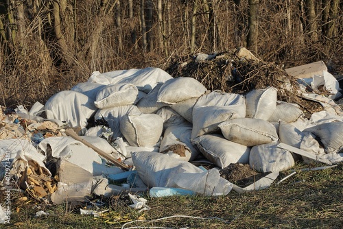 a pile of white garbage bags lie on gray dry grass on nature on a sunny day