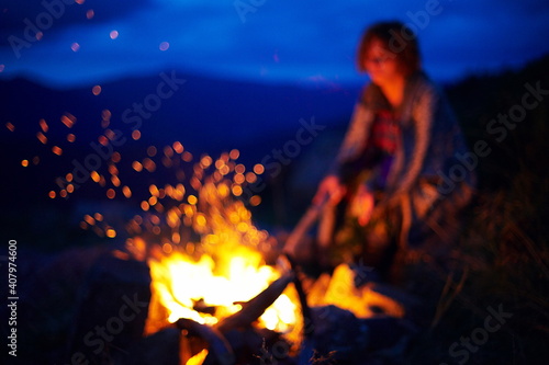 Young caucasian woman near the bonfire at night in the mountains.