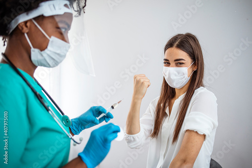 Woman showing thumb up while taking vaccine in medical clinic. Doctor in gloves and face mask holding syringe and making injection to adult female patient. Good advice for illness prevention