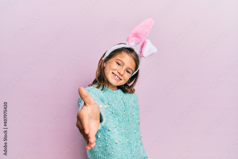 Little beautiful girl wearing cute easter bunny ears smiling friendly offering handshake as greeting and welcoming. successful business.
