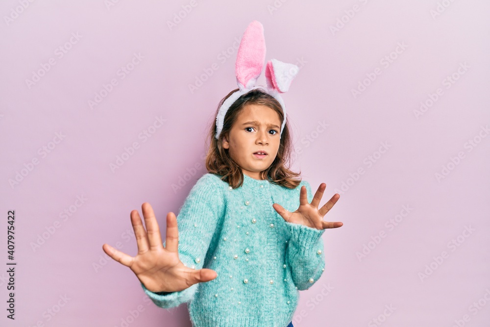 Little beautiful girl wearing cute easter bunny ears afraid and terrified with fear expression stop gesture with hands, shouting in shock. panic concept. Little beautiful girl wearing cute easter bunny ears afraid and terrified with fear expression stop gesture with hands, shouting in shock. panic concept.