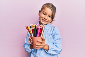 Little beautiful girl holding colored pencils smiling with a happy and cool smile on face. showing teeth.