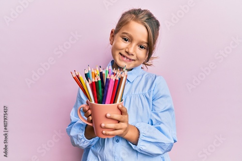 Billede på lærred Little beautiful girl holding colored pencils smiling with a happy and cool smile on face