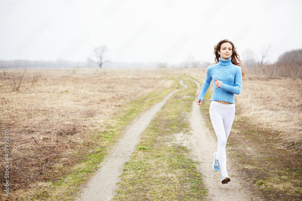 Young caucasian woman jogging in the spring morning in the field